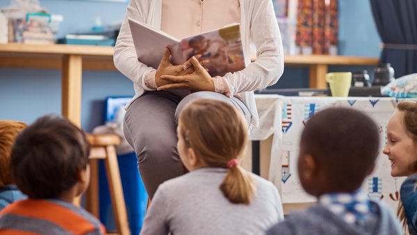 Junge Frau liest einer Gruppe Kinder ein Buch vor.